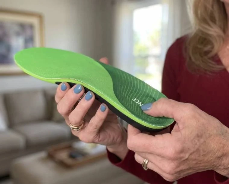 Hands flexing the green XSTANCE insole showing firm arch and soft top layer