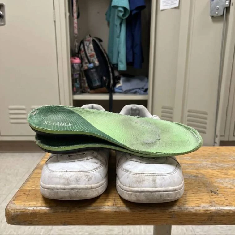 Well-worn green insoles resting on a pair of beat-up work sneakers